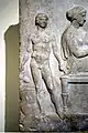 Relieve votivo en el banquete fúnebre. Joven esclavo desnudo sosteniendo un enócoe. Atenas, siglo V a. C.,  Museo Arqueológico Nacional de Atenas.