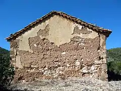 Vista del exterior de la ermita de San Pedro en El Cuervo (Teruel), con detalle del hastial de cabecera y vertientes.