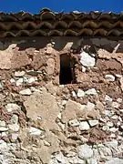 Vista del exterior de la ermita de San Pedro en El Cuervo (Teruel), con detalle de la mampostería del muro meridional, ventanuco y alero.