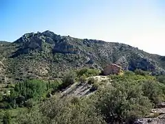 Vista general de la ermita de San Pedro de El Cuervo (Teruel), con la peña de Los Picarzos al fondo.