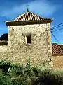 Vista de construcción tradicional (vernacular) en Sesga, Ademuz (Valencia), con detalle del enlucido con mortero de cal en los muros, esquinares de sillería trabada y cubierta a cuatro aguas, correspondiente a la iglesia parroquial. siglo XVI-XVII.