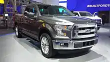 Camioneta Ford F150 de color gris con defensas plateadas en una exposición de Ford con fondo azul.