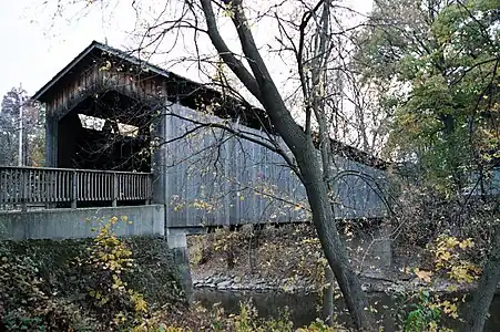 El puente cubierto Ada (1867), en el municipio de Ada. Los extremos de la celosía sobresalen por debajo del revestimiento y la parte superior es visible bajo el techo: esa brecha dejaba entrar la luz permitiendo usar el interior.