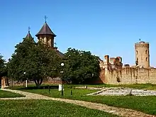 Ruined walls made of stone on a small hill, with a church at the background