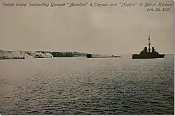 An Italian cruiser bombards two Ottoman ships with smoke billowing over the city.