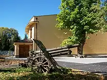 Un bâtiment au mur clair ; au premier plan, un canon.