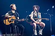 Billie Eilish y su hermano en el escenario de una gira mundial, sujetando sus guitarras acústicas