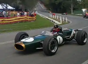 Un coche de carreras verde en forma de puro con ruedas sin carenar y cabina abierta. El número uno está pintado en morro y los costados.