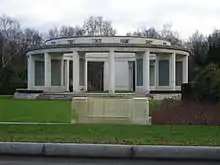 Open white stone circular structure, supported by broad columns carrying inscribed tablets.