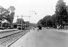 A photograph with a streetcar on the left and a city street with pedestrians crossing on the right