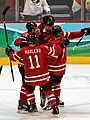 Varios jugadores de la selección canadiense de hockey sobre hielo celebran un gol dándose un abrazo.