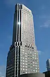 Ground-level view of a beige, multi-faceted, window-dotted high-rise