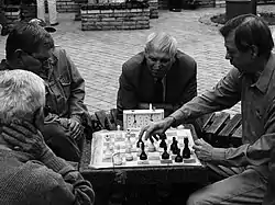 La foto muestra dos hombres jugando al ajedrez mientras otros dos miran.