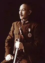 A Chinese man in military uniform, smiling and looking towards the left. He holds a sword in his left hand and has a medal in shape of a sun on his chest.