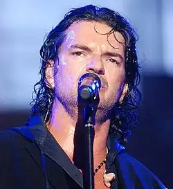 Ricardo Arjona, cantando en un micrófono.