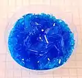 Cristales de CuSO4 pentahidratado creados artificialmente en un vaso plástico.