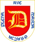 En campo de gules, una letra D de oro, con unas flores de plata, bordura de plata y, en letras de azur, la salutación angélica "Ave María gratia plena". En campo de azur una cruz llana de oro.