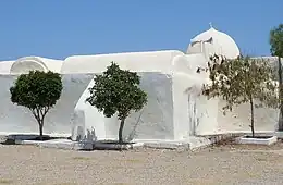 Façade de la mosquée Essatouri vue de l’extérieur et coiffée d’une coupole ; trois arbustes sont plantés au premier plan.