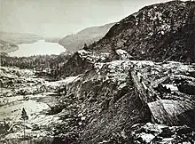 Lake beside snowy mountains with railroad construction sheds in foreground.