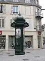 Una columna Morris en Épinal, con una fuente decorada con un mascarón en forma de cabeza de león.