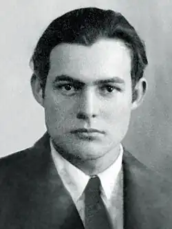 Vista frontal de un joven con cabello moreno, ojos oscuros, vestido con camisa, corbata y chaqueta.