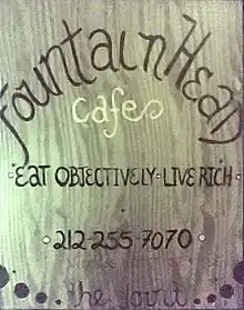 Una señal de madera muestra las palabras "Café Manantial: Come objetivamente, vive rico"