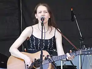 Welch singing and playing guitar on stage, wearing a black dress