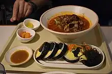 Gimpap servido junto a sopa picante y banchan de kimchi. También hay salsa y jengibre. Un gimbap contiene alga.