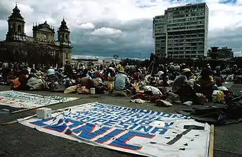 Plaza Mayor de Guatemala, ejemplo de Plaza de Armas, con la catedral colonial y edificios de arquitectura del siglo XX. La función de acoger el conflicto social, como esta manifestación, es también propia de los espacios abiertos urbanos.