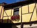 Entramado de madera, enfoscado en tonos ocres, única ventana con petunias rojza.