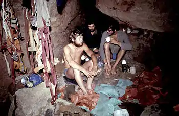 Three people sitting down at an underground camp site surrounded by their equipment