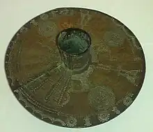 Tobillera realizada de una barra de latón macizo del tipo que usan las mujeres Igbo. Ahora en la colección de Wolverhampton Art Gallery. El tubo de la pierna se extiende unos 7 cm a cada lado del disco de 35 cm.