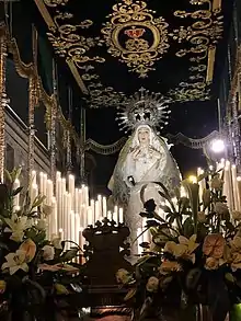 Virgen de la amargura en su trono rodeada de velas y de ramos de flores