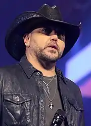 Jason Aldean con atuendo y sombrero negros sosteniendo un micrófono