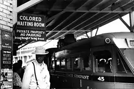 A train station platform, with a sign: Colored Waiting Room