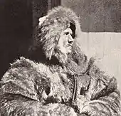  Head and upper body of a man, facing right. He is dressed in heavy fur clothing including a hat which conceals much of his face, although the profile is clear