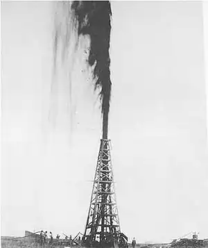 Photo of a black substance gushing high over an oil rig.