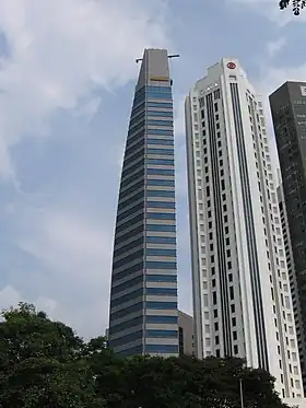 Ground-level view of two 40-storey towers. The building on the left is very thin with a blue and grey facade. The building on the right has a square cross section with diagonal, cut-off corners and a tapering roofline.