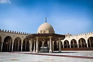 Photo of a paved courtyard surrounded by an arcade, with a domed pavilion in the centre over a well