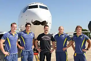 Miembros de la Selección de rugby de Australia llevando bigote en la presentación de un Boeing 737-800 de Qantas decorado para Movember.