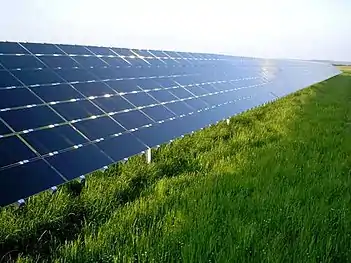 Los paneles solares, con un ángulo de unos 30 grados, reflejan el cielo azul por encima de un campo cubierto de hierba.