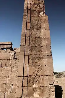 Apedemak emergiendo de una flor de loto en forma de serpiente con cabeza de león