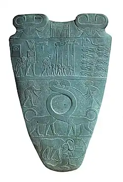 Reverso de la Paleta de Narmer, hacia el 3100 aC. La fila superior representa a cuatro hombres que llevan estándares. Sobre ellos es un Serej que contiene el nombre del rey, Narmer.