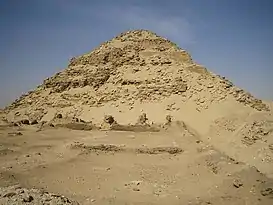 Ruins of a pyramid, its shape well preserved, in the desert.