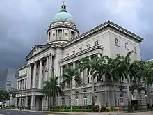 A dome sits atop this building, which is next to a road. The building's large entrance stands at its centre and is fronted with pillars.