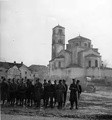 Des hommes en arme sur une place de la ville, avec des bâtiments en arrière-plan.