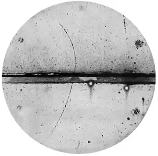 track of subatomic particle moving upward through cloud chamber and bending left (an electron would have turned right)