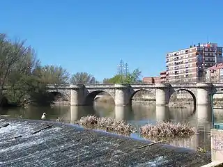 La foto muestra un puente de piedra con cinco arcos sobre el río.