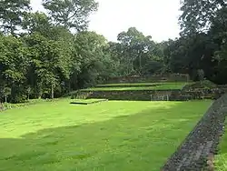 Una superficie plana bordeado por árboles y cubierta de hierba, con estructuras bajas al otro lado.