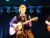 El cantante de música country Rodney Crowell, sentado en un taburete y tocando una guitarra acústica